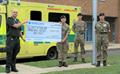 Man in EEAST unfiform receiving a cheque from three people in camouflage uniform.